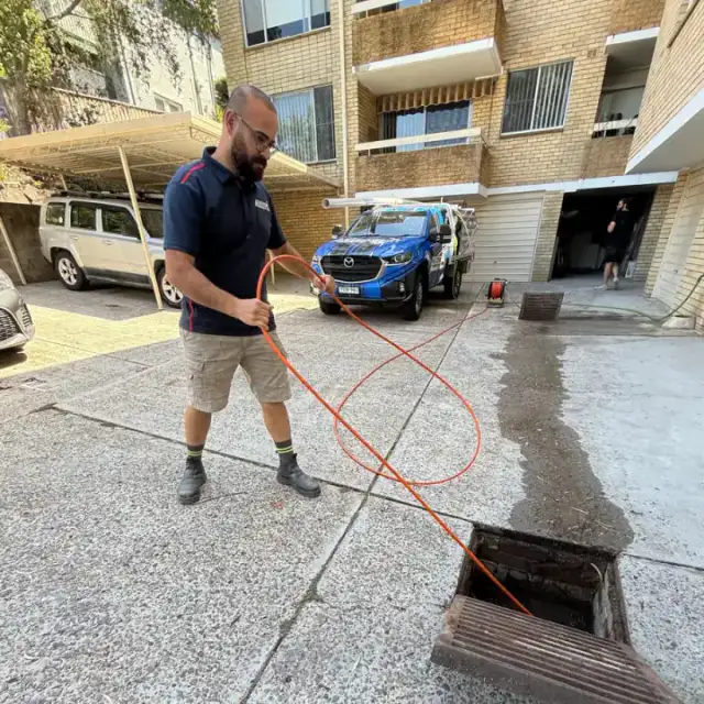 Antons technician using a drain-clearing hose at an outdoor access point