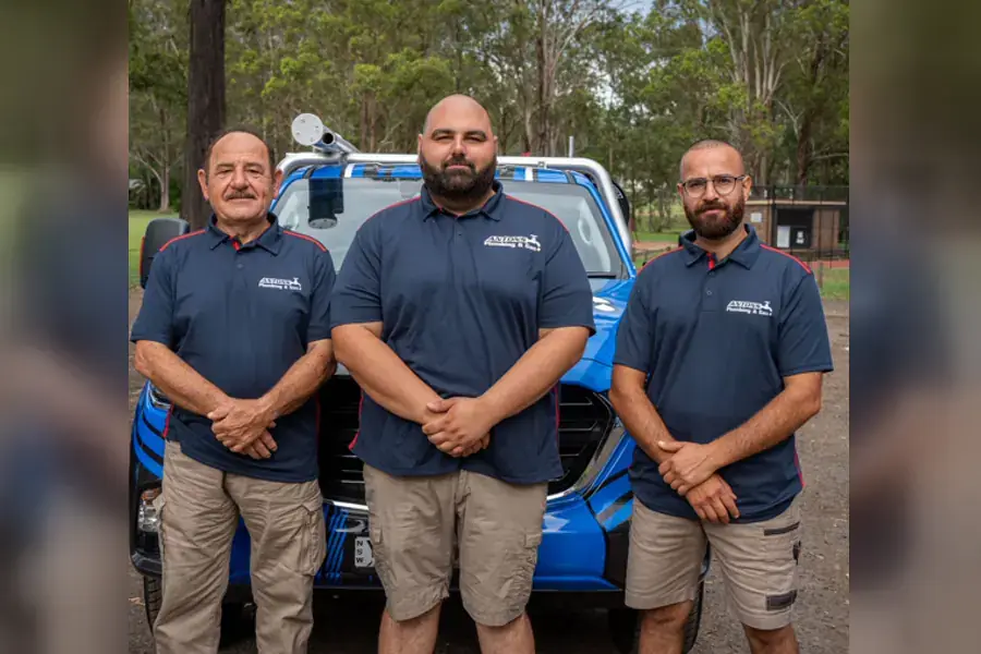 Three licensed plumbers standing beside a blue service vehicle