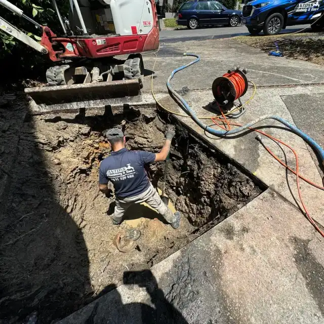 Drain excavation beside a driveway with pipe inspection equipment nearby