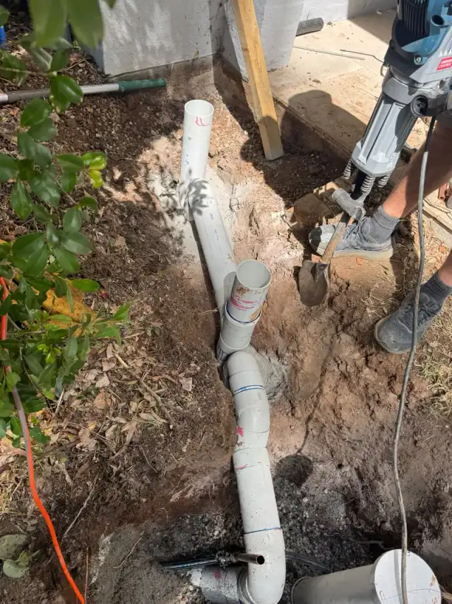 Exposed drainage pipe within an excavation beside masonry